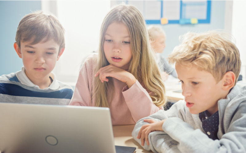 Three young learners working together on a laptop
