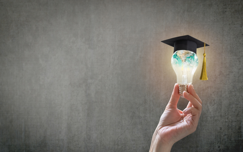 Hand holding a lightbulb wearing a graduation cap