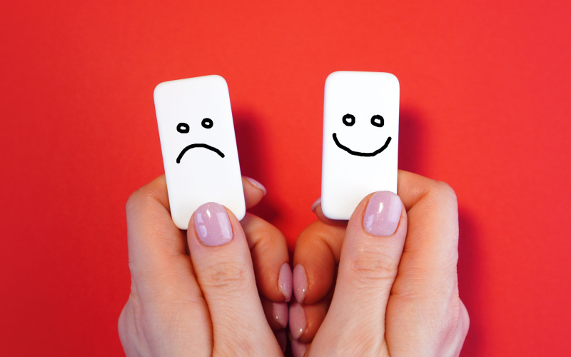 Hand holding two white tiles with happy and sad faces drawn on