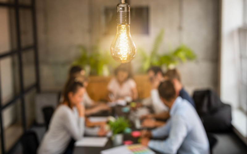 Image of a lit lightbulb with a team of people blurred in the background