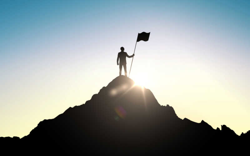 Silhouette of businessman with flag on mountain top over sky and sun light background